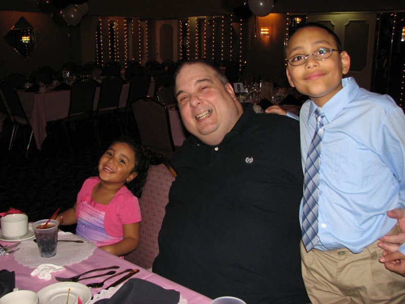 Man smiles with two children at a table, likely at an event.