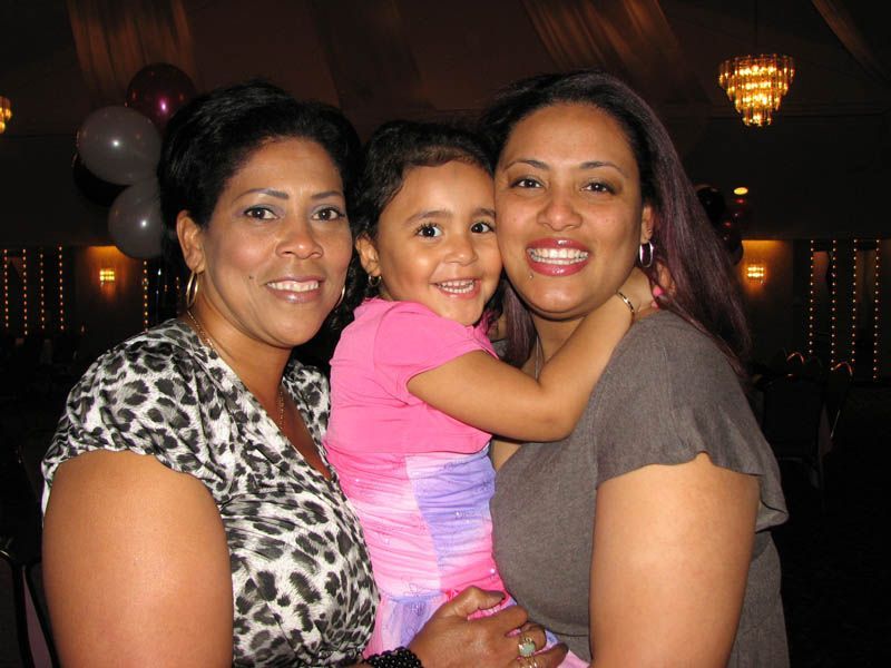 Two women and a child smiling, hugging at an event. The child wears pink and purple. One woman has a leopard print top.