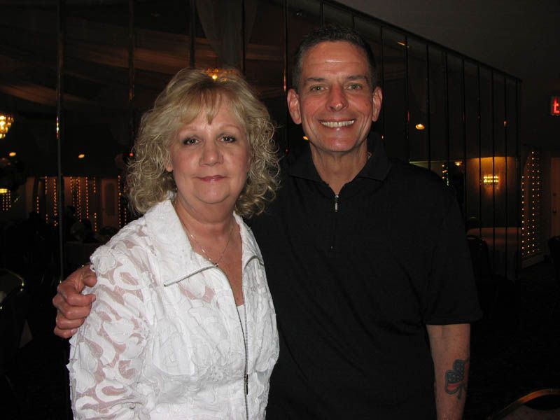 Woman in white shirt and man in black polo shirt smile, posing indoors.