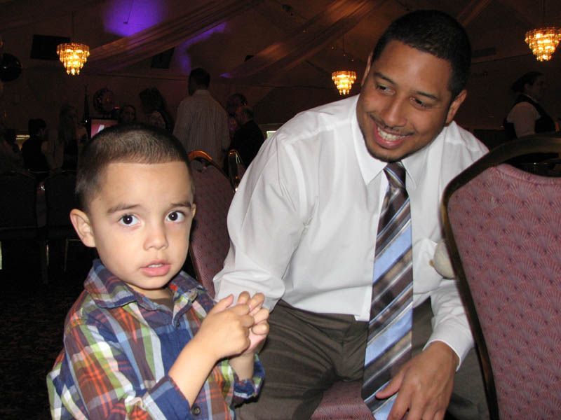 A man smiles at a child while holding his hand. They are indoors in a room with chandeliers.