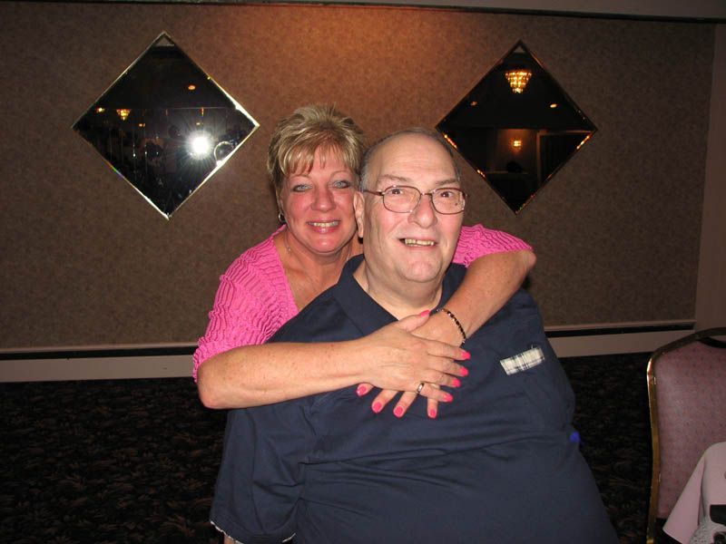 Woman hugging a man; both smiling. Pink top, blue shirt. Mirrors in background.