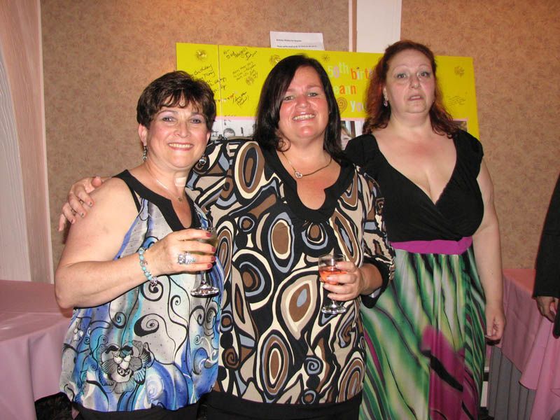 Three women in festive attire at an event, smiling and holding drinks.