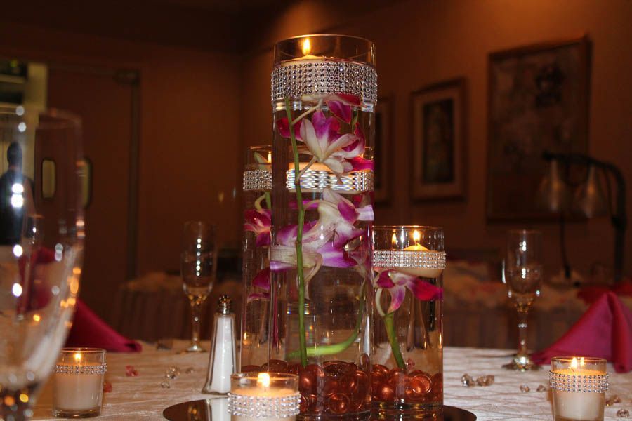 Centerpiece of orchids in vases, candles, table setting, indoor.
