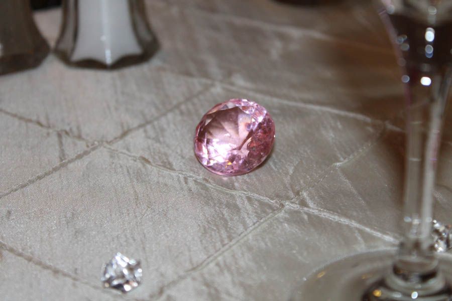 Pink gemstone on a white tablecloth, salt shakers and a wine glass in the background.