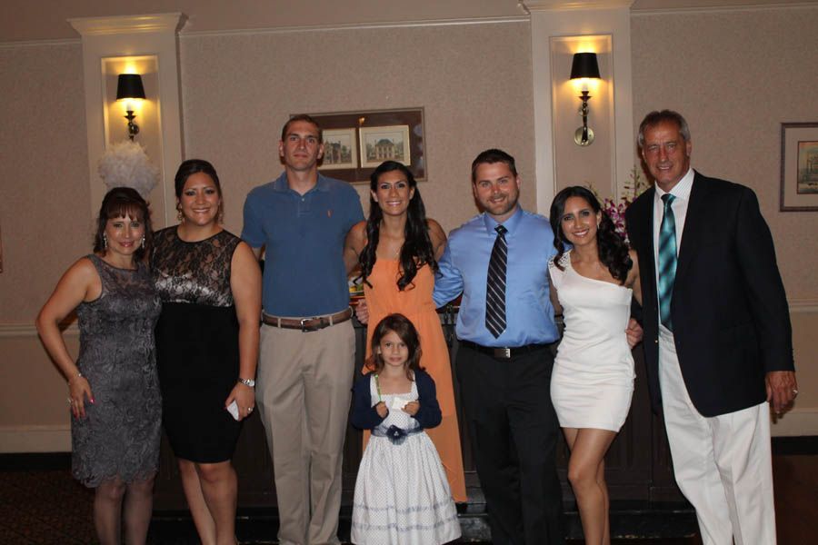 Group of eight people posing indoors. Formal wear, neutral background.