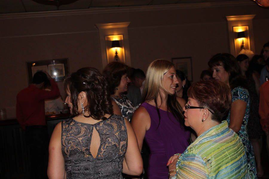 People in dresses gather and chat in a warmly lit room; some have drinks.