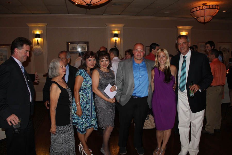 Group of people at an indoor event, some posing for the photo. Men in suits, some women in dresses.