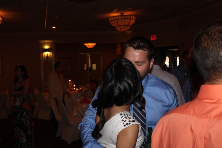 Couple kissing on a dance floor, man in blue shirt, woman in white dress, indoor reception.