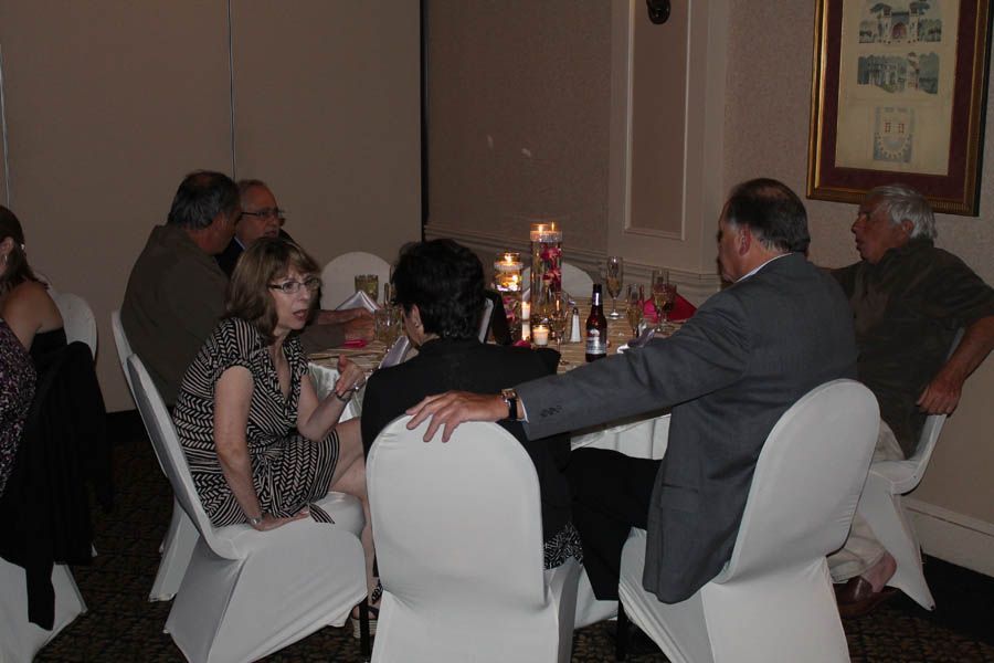 People seated at a round table, lit by candles, engaged in conversation. Formal setting.