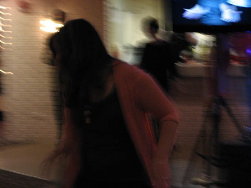 Woman in pink sweater and dark clothing dancing at a party, blurred motion.