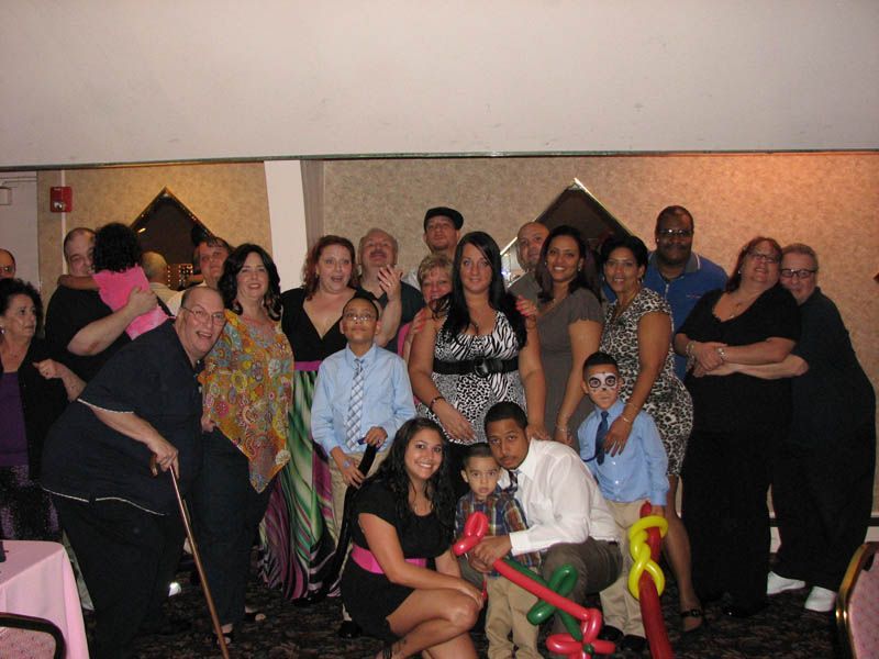 Group of people posing for photo at a party; indoors, several children, woman in a leopard print top.