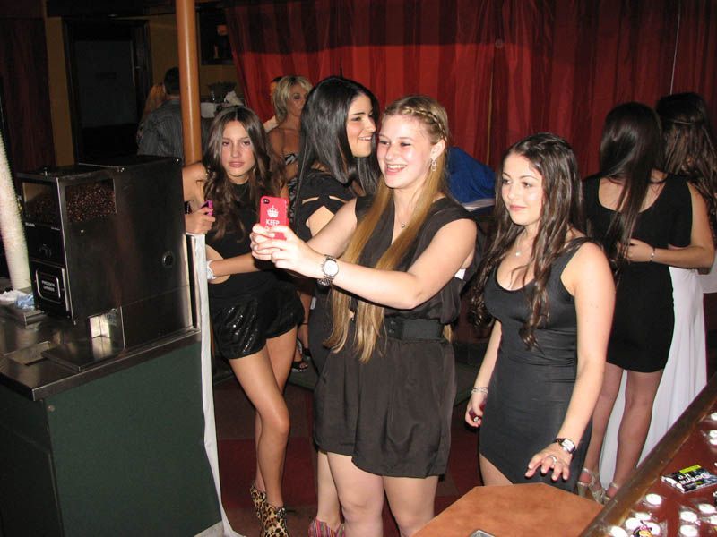 Group of young people in black outfits take a selfie inside a venue with red curtains.