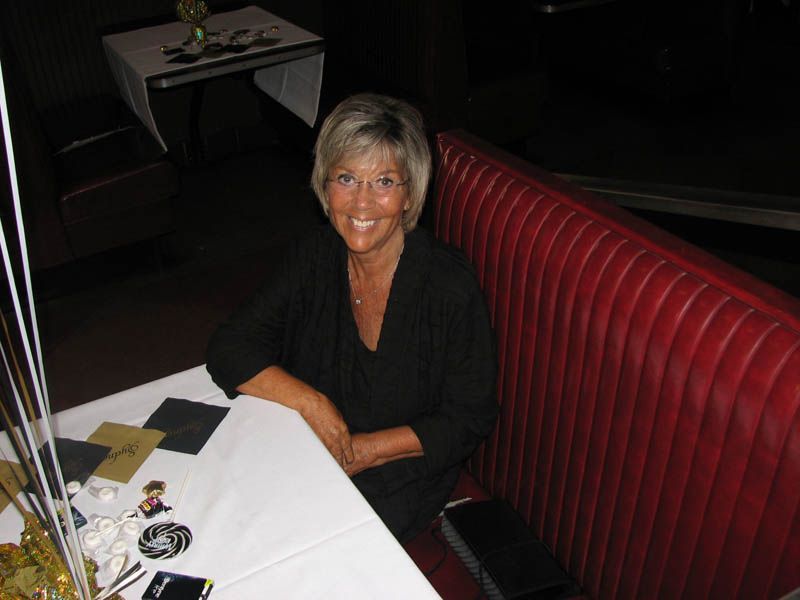 Woman seated in a red booth at a table, smiling. Restaurant setting.