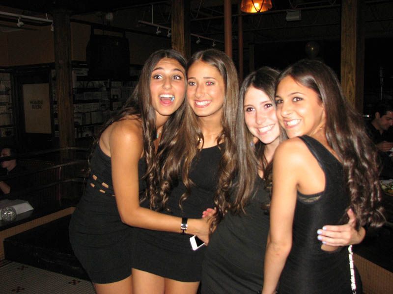Four women in black dresses smiling and posing indoors.