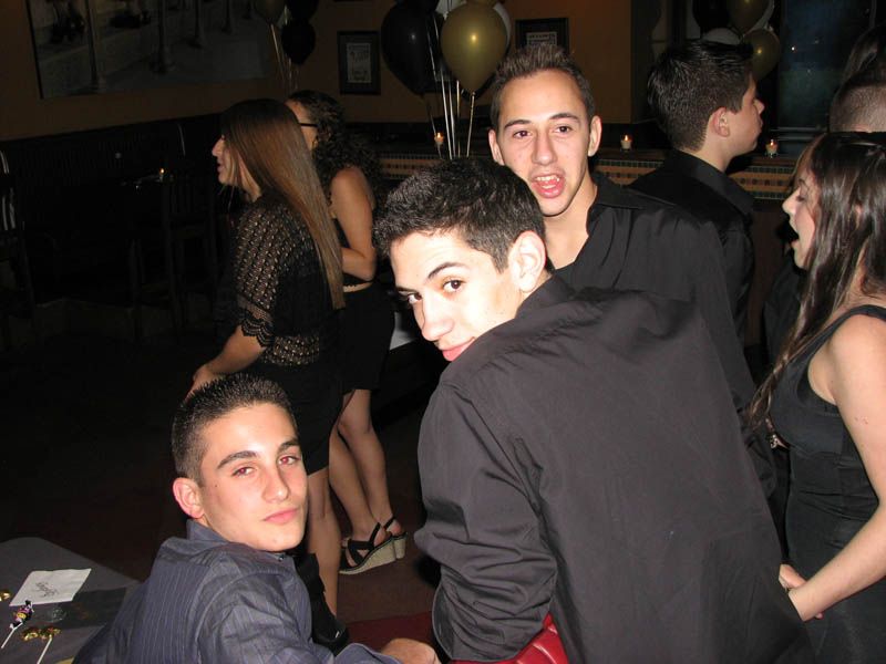 Group of young people in dark attire at a party, looking at the camera with various expressions.