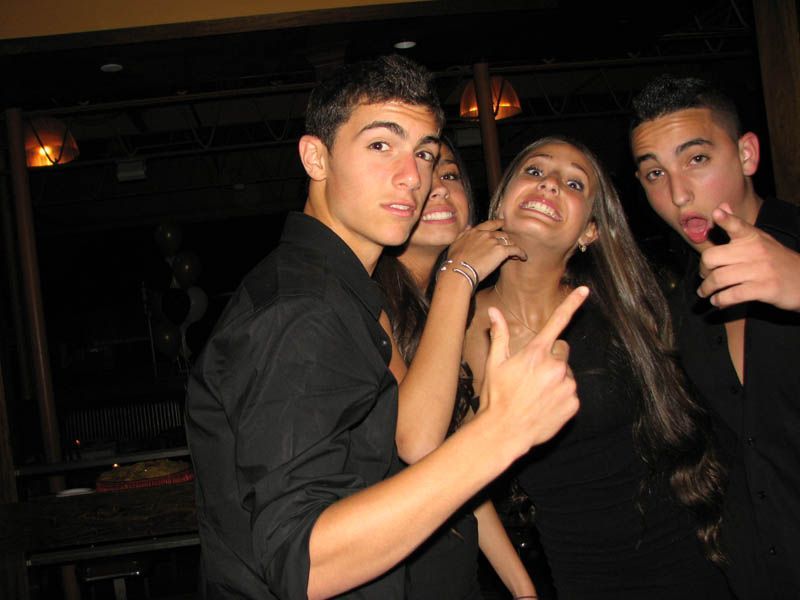 Four people in a dimly lit setting. Two men and two women pose with various hand gestures and expressions.