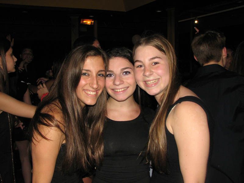 Three young people smile at the camera at a dimly lit event.