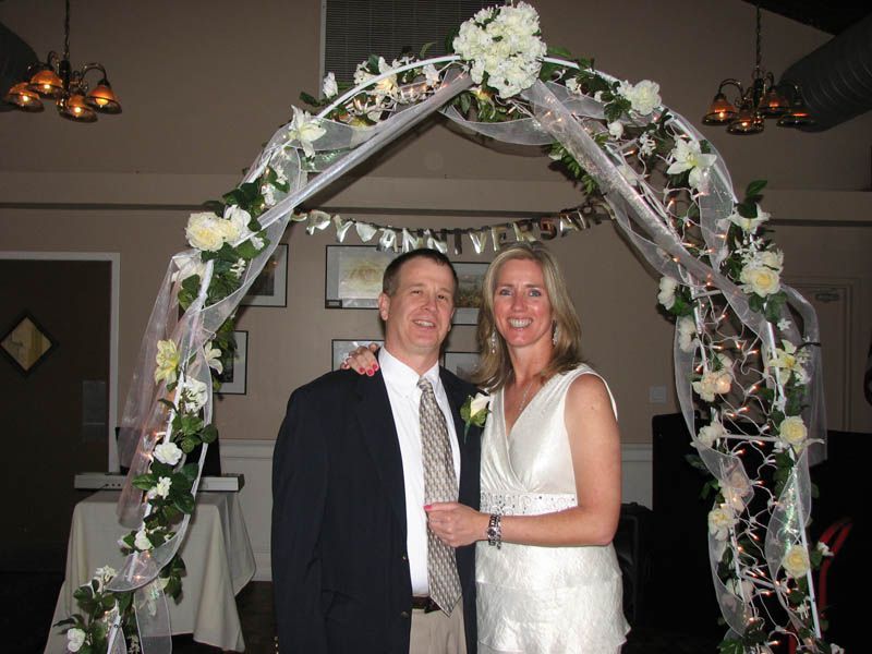 Couple stands under a decorated wedding archway.
