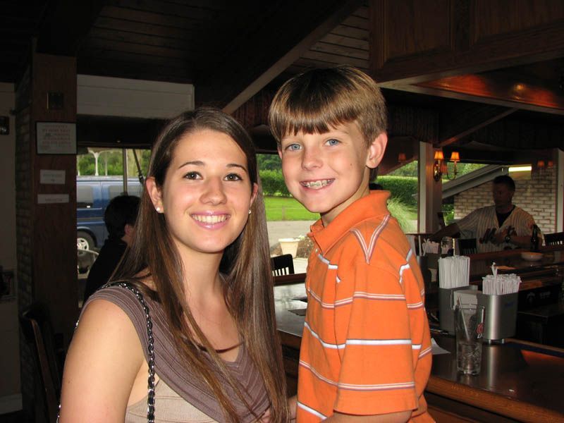 Woman and young boy smiling near a bar. The boy wears orange and white striped shirt. Interior setting.
