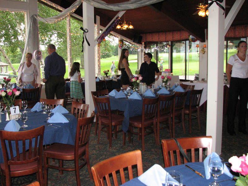 Reception hall with tables set for guests, blue linens, and people mingling.