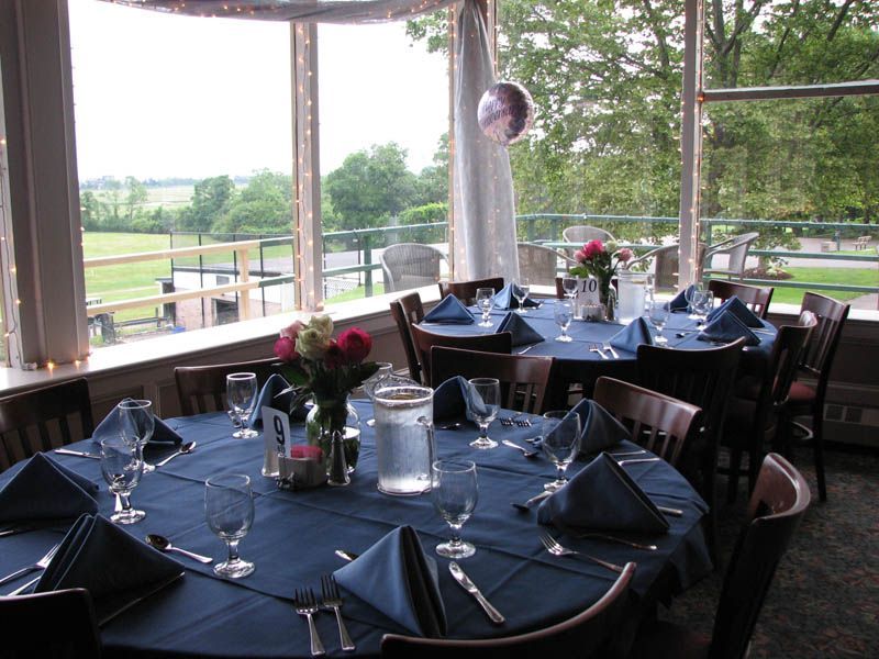 Dining tables set for a party, with blue tablecloths and floral centerpieces, overlooking a green landscape.