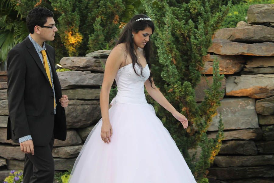 Bride in a white gown and groom in a suit near a stone wall and greenery.