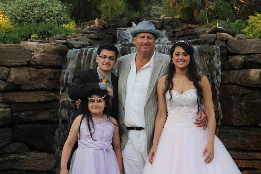 Family poses in front of a waterfall: two young adults, a girl, and a man in a hat.