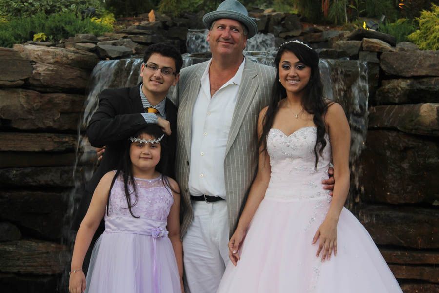 Family posing by waterfall: formal dresses, suit, and hat.