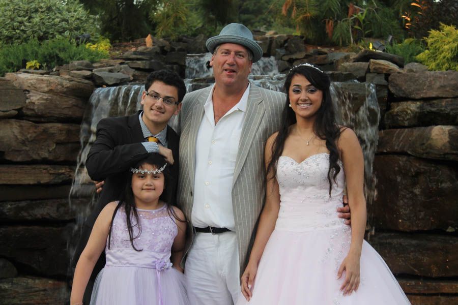 Family posing in front of a waterfall: woman in a white dress, man in a suit, two children in formal wear.