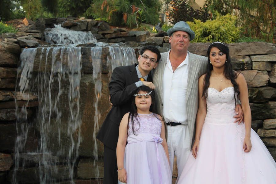 Family posing by a small waterfall. Formal wear: suits, white dress, and a lavender dress.