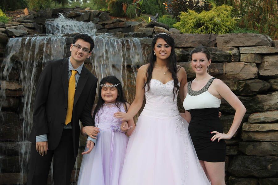 Four people pose in front of a small waterfall. One woman in a white dress, others in formal wear.