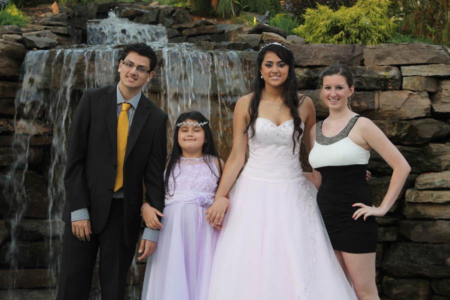 Four people pose in front of a waterfall: formal attire includes a suit, two dresses, and a flower girl.