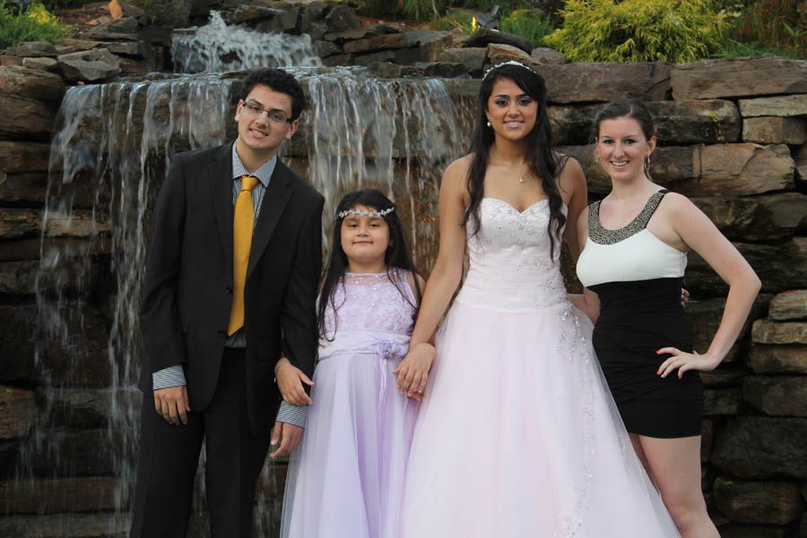 Four people stand in front of a small waterfall. A man in a suit, a girl in a dress, and two women.