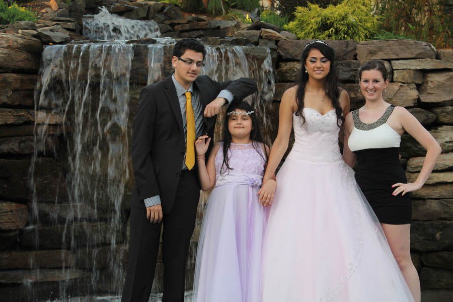 Four people pose near a waterfall: a man, two women, and a young girl. The women are in formal dresses.