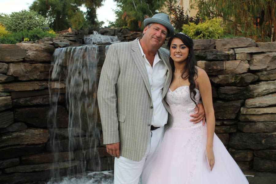 Man in light suit and woman in pink gown pose by a waterfall.