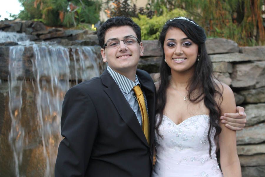 Couple posing by a waterfall. Man in suit and tie; woman in strapless white dress and tiara, both smiling.