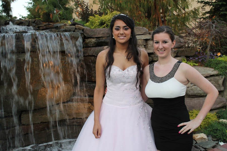 Two women pose by a small waterfall. One wears a white formal dress, the other a black and white dress.