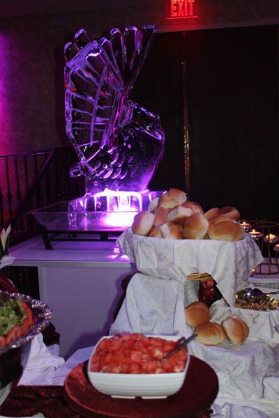 Ice sculpture lit with purple light above a buffet. Bread rolls, salsa, and other food items are displayed.