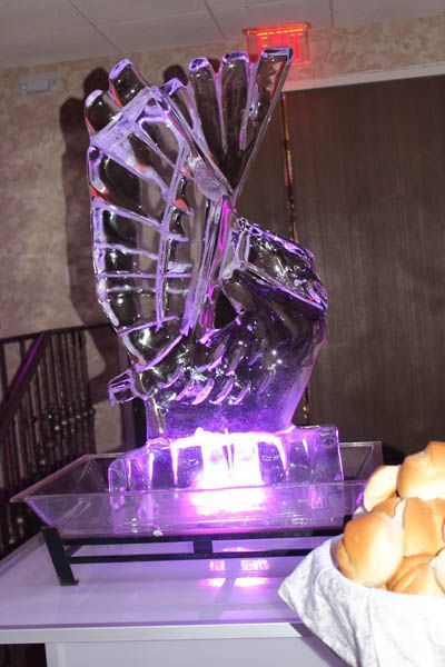 Ice sculpture lit with purple light, atop a serving table near a basket of bread rolls.