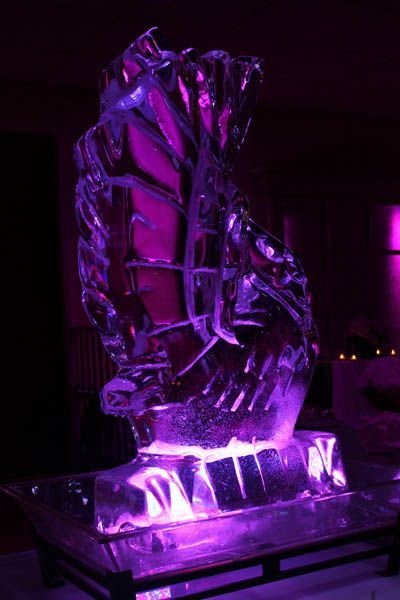 Ice sculpture of a seahorse, illuminated with purple light, displayed on a table.