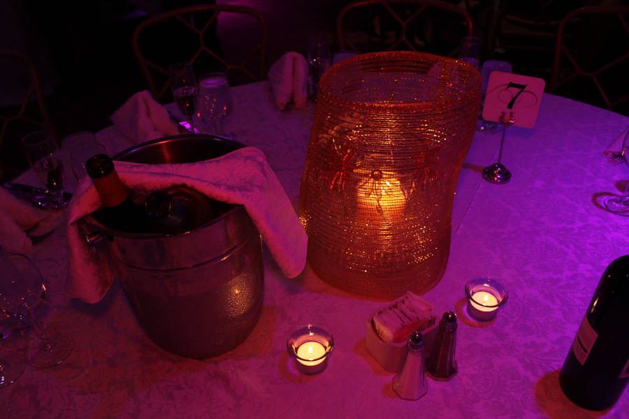 Table setting with champagne bucket, large orange vase, candles, and table number 7 under purple lighting.