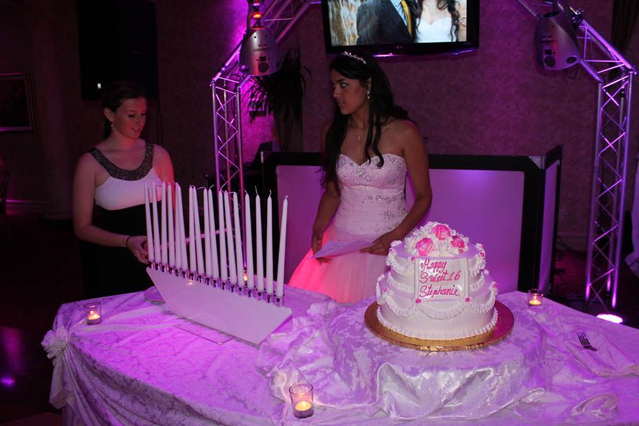 Girl in white dress with cake and candles at a party with purple lighting.