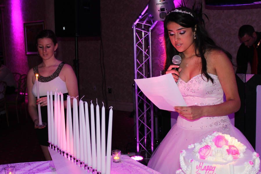 Girl in formal dress speaks at a party with candles and cake, while another holds a candle.