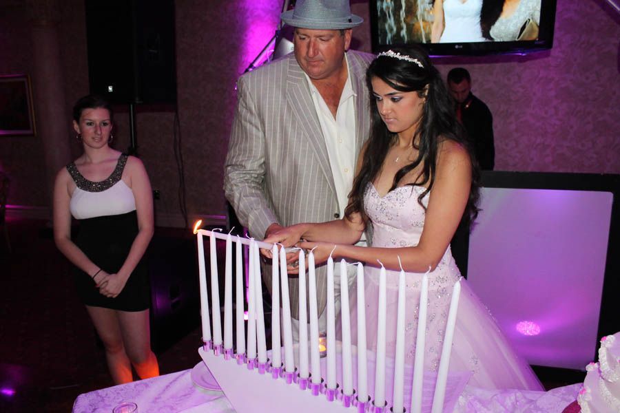 Girl in gown with man lighting candles at a party. Woman looks on. Purple lighting.