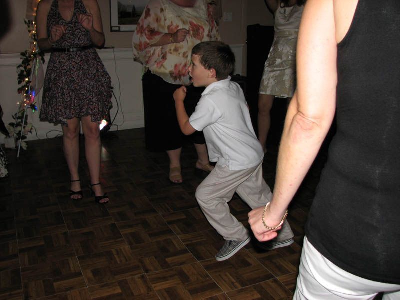 Boy dancing at an event, wearing a light blue shirt and khaki pants. People in background.