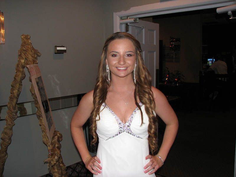 Woman in white formal dress smiling, hands on hips, near doorway.