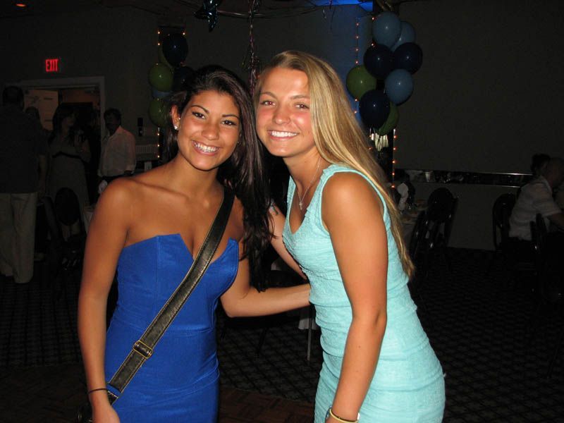 Two young women smiling at a party. One in blue dress, other in light blue. Balloons in background.