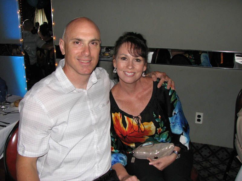 Man and woman with arms around each other, smiling. Man in white shirt, woman in floral top. Inside.