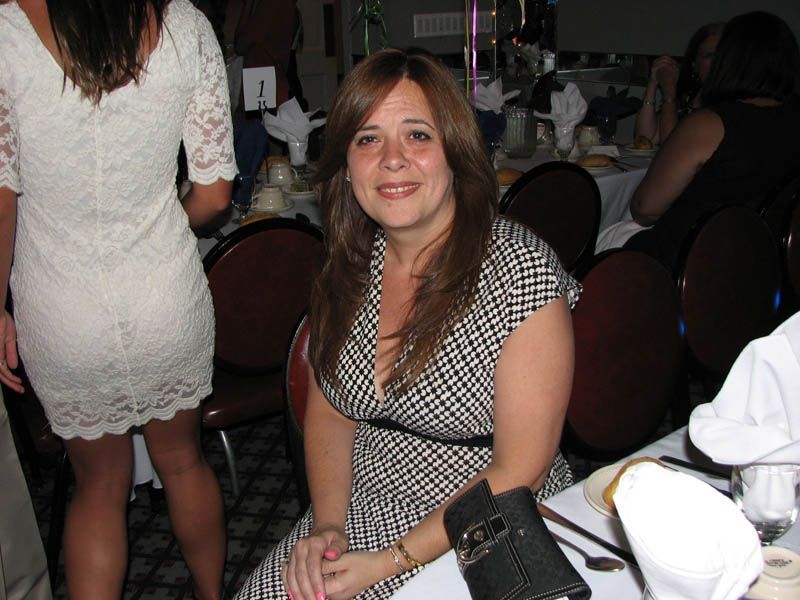 Woman in a black and white patterned dress, seated at a banquet table, smiling.