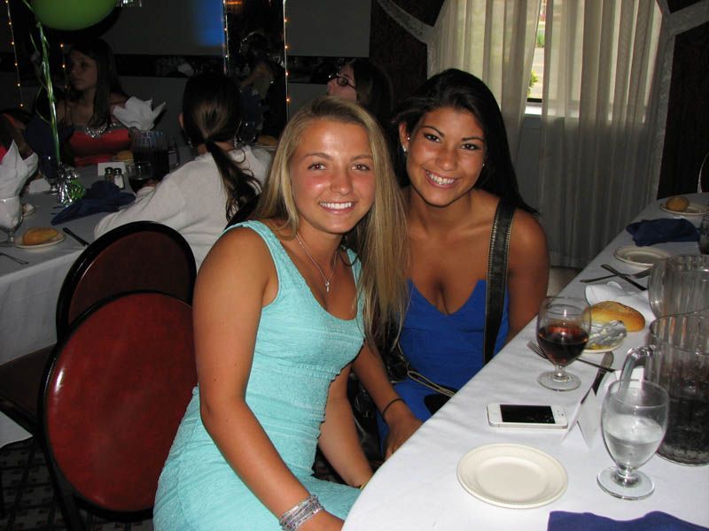 Two women seated at a table, smiling. One in blue dress, one in aqua, at an event.